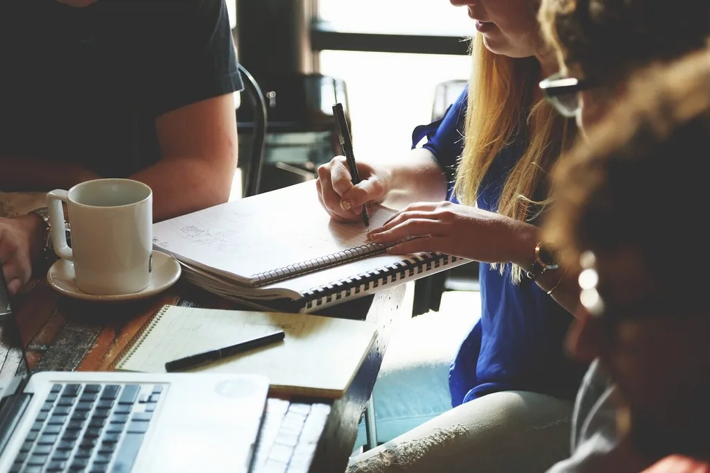 Marketing meeting with people around a table, mugs, pads and laptops